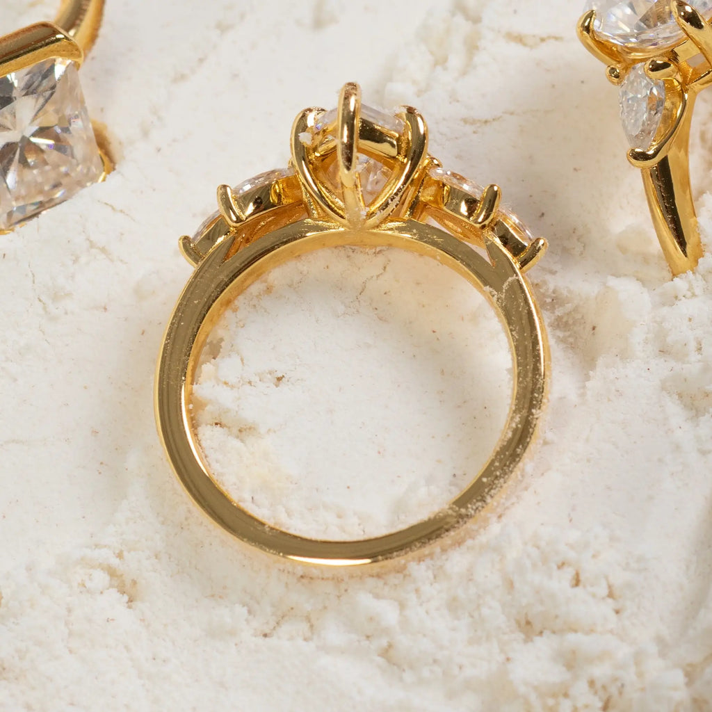 Detalle lateral del anillo de compromiso corte marquesa con diamantes laterales en diseño cluster y estructura elevada en oro amarillo